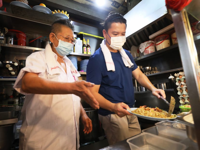 Mr Kang Kaiming (left) showing his mentee Louis Wong how to serve Hokkien prawn noodles at Geylang East Market and Food Centre.
