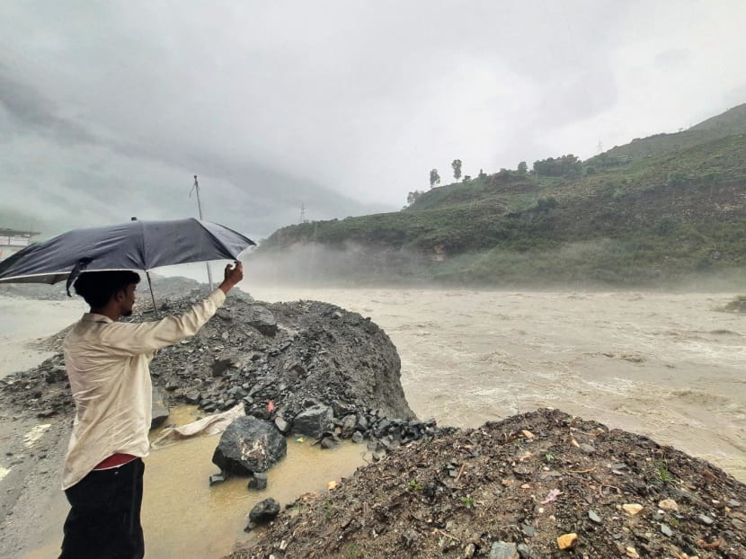 In this photograph taken on July 9, 2023, a man holds an umbrella while standing on the banks of swollen river Satluj after heavy monsoon rains in Rampur, in India's Himachal Pradesh state.