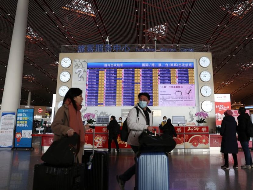 Travellers walk with their luggage past a display showing departure flight information at the Beijing Capital International Airport, during the Spring Festival travel rush ahead of the Chinese Lunar New Year, in Beijing, China on Feb 2, 2024.
