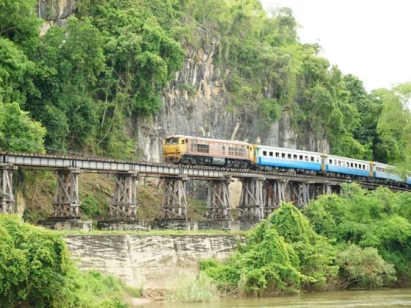A train passes a famous wooden bridge on the Death Railway in Kanchanaburi province, Thailand.
