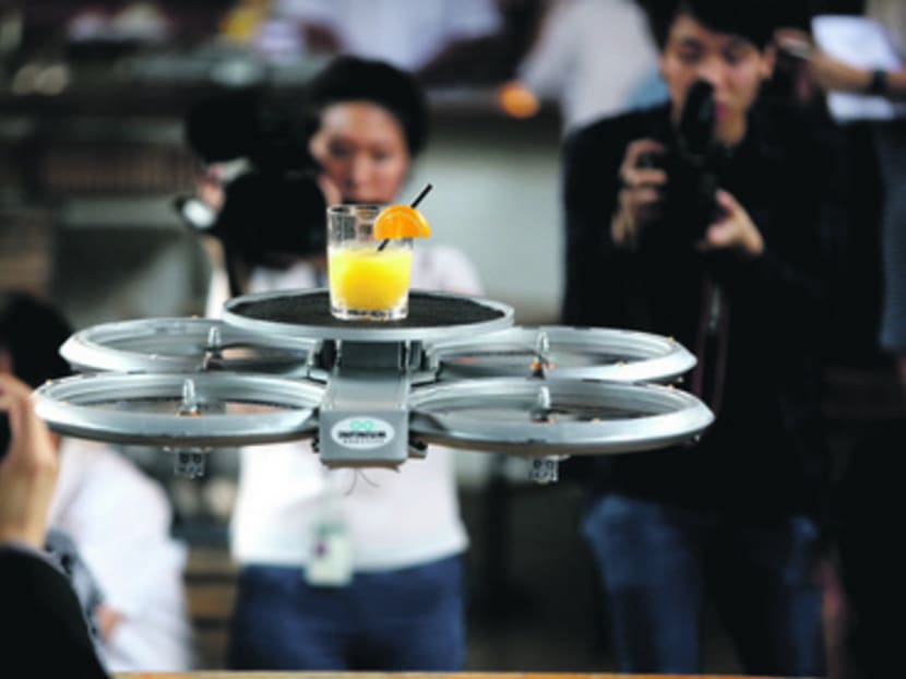 An Infinium-Serve flying robot sending an order of orange juice hovers above a table as it readies to land during a media demonstration at Timbre @ The Substation.