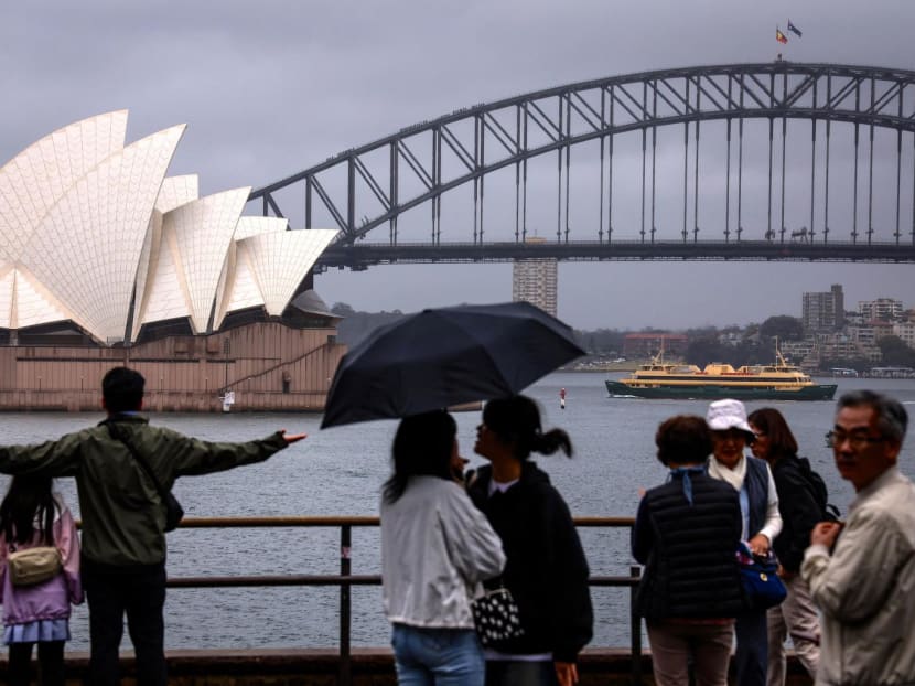 Tourists hold umbrellas and take photographs of the Sydney Opera House on a rainy day in Sydney on Dec 21, 2023.