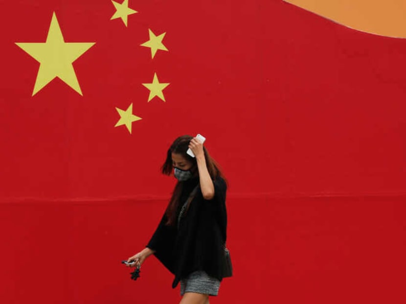 A woman wearing a mask walks past a wall painted with China's national flag in central Beijing.
