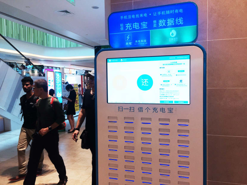 Customers walk past phone chargers of a phone charger sharing service to be rented at a shopping mall in Shanghai, China on 20 May, 2017. Customers walk past phone chargers of a phone charger sharing service to be rented at a shopping mall in Shanghai, China on 20 May, 2017.