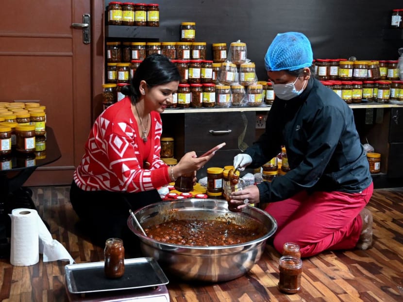 Nepali influencer Anjana Aryal (left) uses her phone while packing pickles, at her residence in Lalitpur, Nepal on Dec 4, 2023.