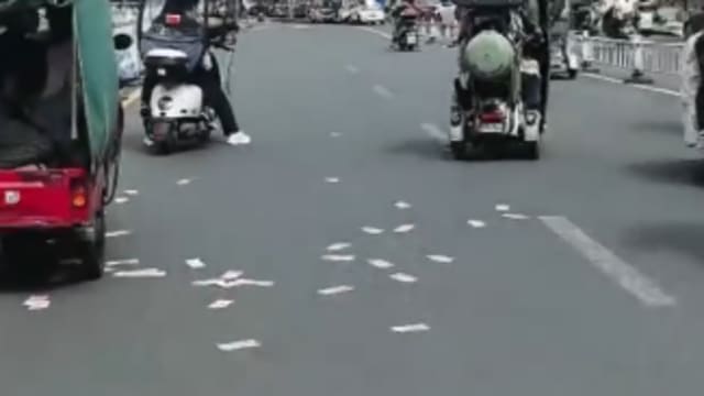 中国男子骑车掉钞票 钱洒满地路人围捡 