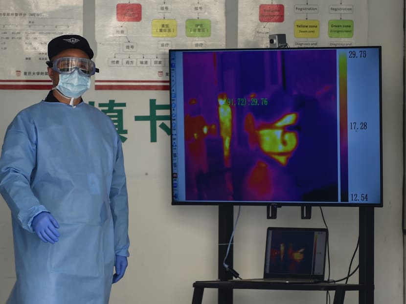 A security guard wearing protective clothing is seen next to footage from a thermal camera at an access point to Huashan Hospital in Shanghai on Feb 27, 2020.