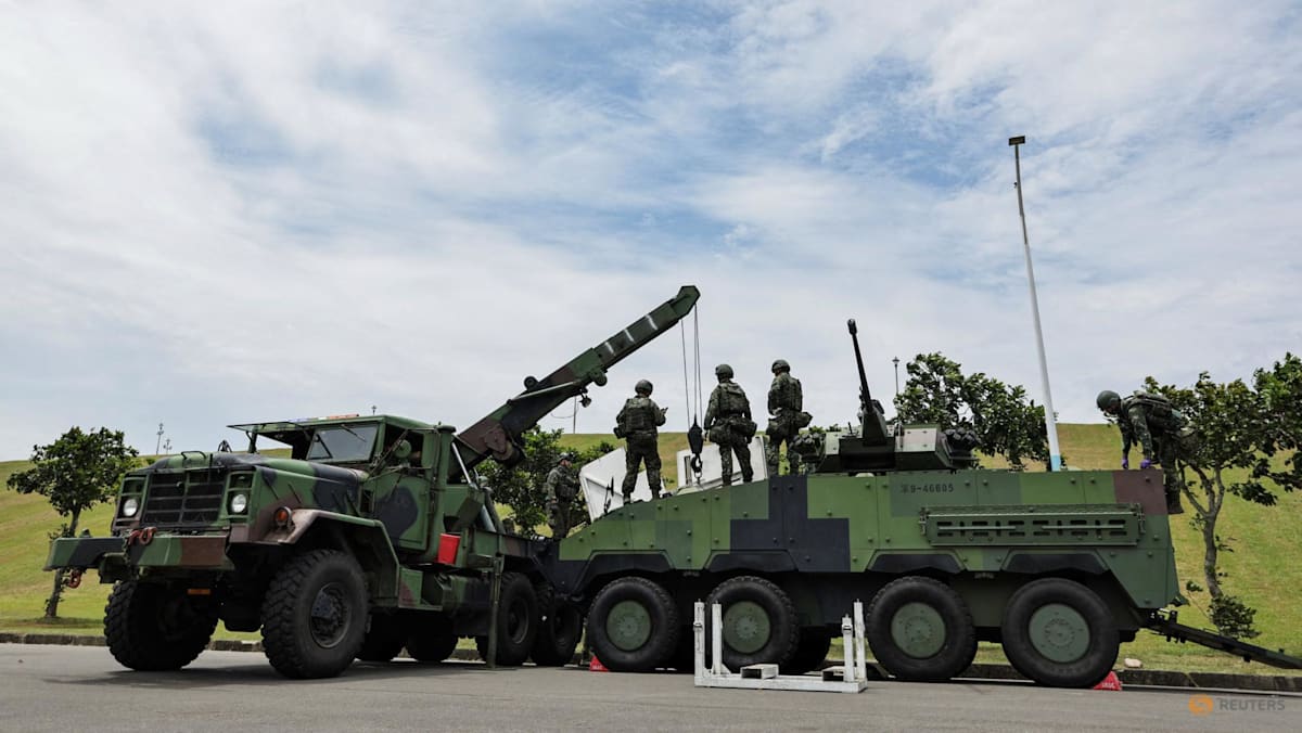 Military personnel stand near two camouflaged military vehicles outdoors.