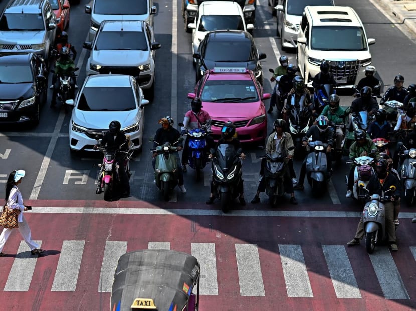 Motorcyclists wait under the shade as a woman crosses a traffic intersection in Bangkok on April 25, 2024. Motorcyclists wait under the shade as a woman crosses a traffic intersection in Bangkok on April 25, 2024.