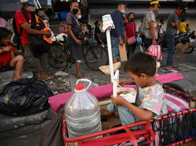 In this photo taken on Nov 24, 2020, a child sits on the family's tricycle and eat free packed meals distributed by Catholic religious order Society of the Divine Word in Manila.