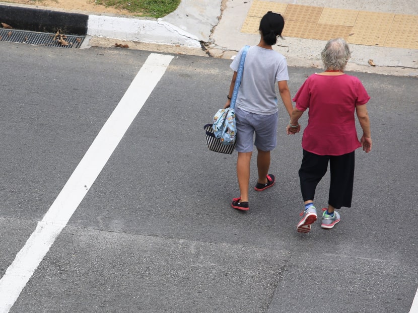 A maid holding the hand of an elderly woman while crossing the road. TODAY file photo