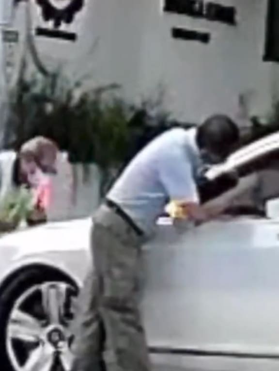 A screenshot from a video showing a security officer and a staff member of Red Swastika School preventing a car from entering the school compound.