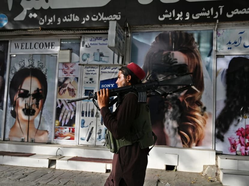A Taliban fighter walks past a beauty salon with images of women defaced using spray paint in Shar-e-Naw in Kabul on Aug 18, 2021.