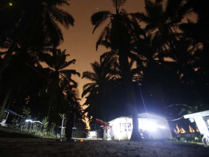An immigrant enforcement officer stands outside makeshift shelters of migrant workers, as light trails of torches used by the officers during their search for hiding illegal workers are seen, during a crackdown on illegal migrant workers in a palm plantation in Nilai, outside Kuala Lumpur on Sept 1, 2013.