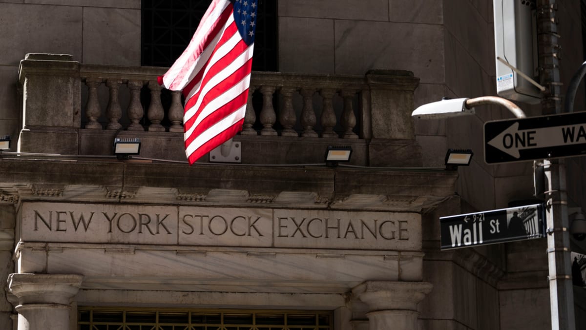 The entrance of the New York Stock Exchange building with an American flag and street signs for Wall Street.