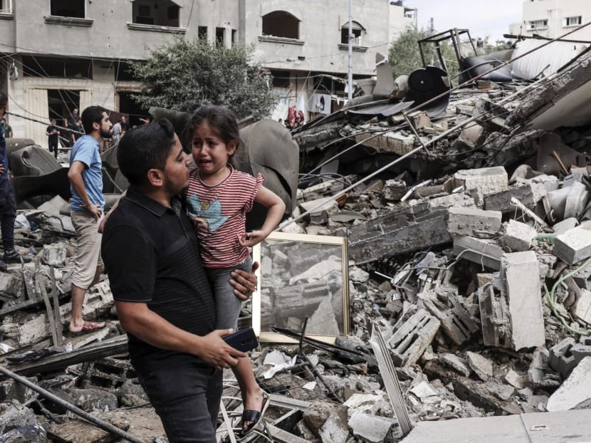 A man carries a crying child as he walks in front of a building destroyed in an Israeli air strike in Gaza City on October 7, 2023.