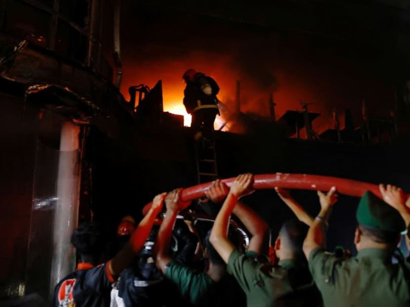 Volunteers carry a water pipe as firefighters spray water to douse the fire after a fire that broke out in a multi-storey building in Dhaka, Bangladesh, on Feb 29, 2024.