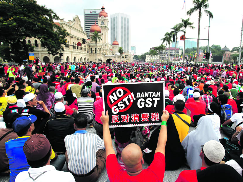 A protester holds up a placard as others sit in front of the historical building of Sultan Abdul Samad during a protest against the implementation of the Goods and Services Tax (GST) in Kuala Lumpur, Malaysia, Thursday, May 1, 2014. Photo: AP