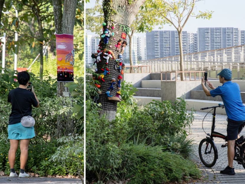 Passers-by at Jurong lake Gardens stopping to take photos of knitted craft displays wrapped around tree trunks. 