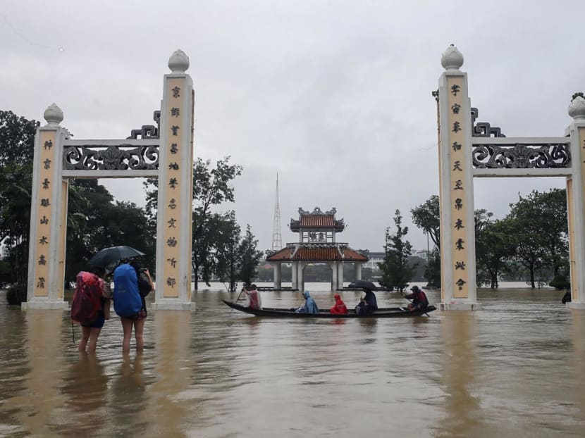 People ride on a boat and walk through a flooded area of Hue city in central Vietnam on Nov 15, 2023.