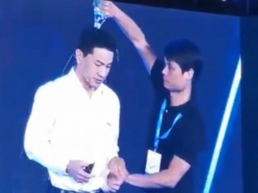 Baidu founder Robin Li looks shocked as a man from the audience pours a bottle of water over his head.