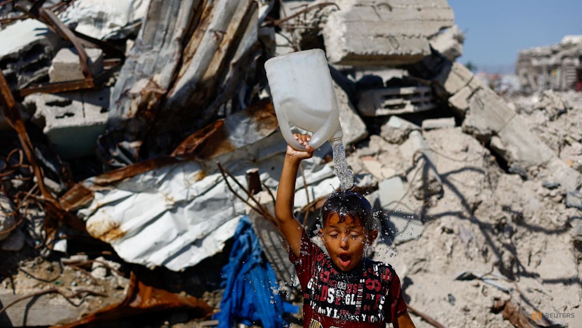 A child holding a bottle of water amidst a scene of rubble.