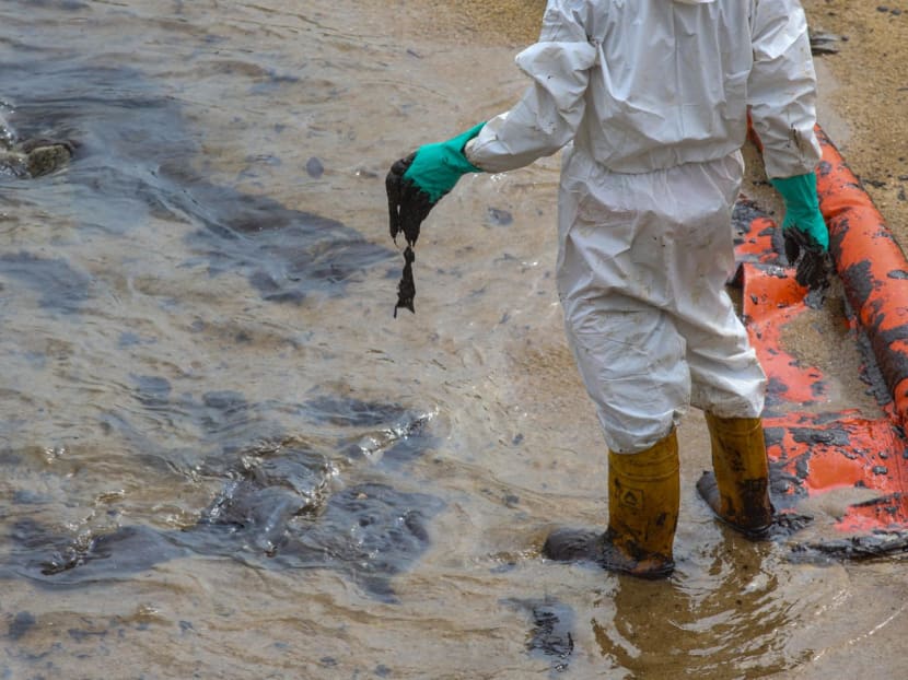 Workers cleaning up sand covered in oil at the beach at East Coast Park on June 18, 2024.