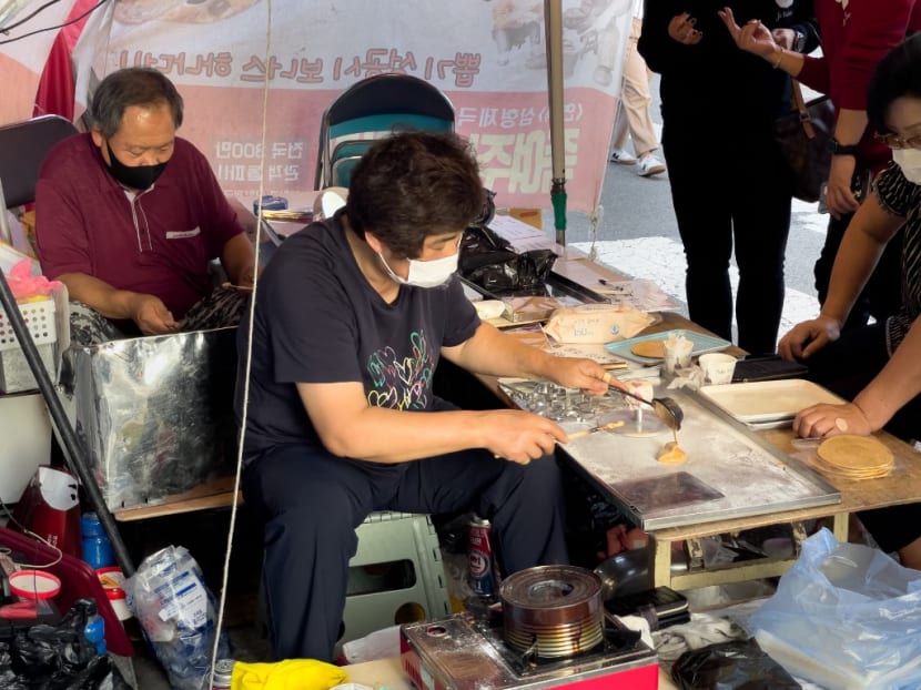 In this picture taken in Seoul on Oct 10, 2021, customers wait in line as street vendor Jung Jung-soon and her husband Lim Chang-joo sell freshly made dalgonas, a crisp sugar candy featured in the Netflix smash hit series Squid Game, for which they were hired to be on set to make during production.