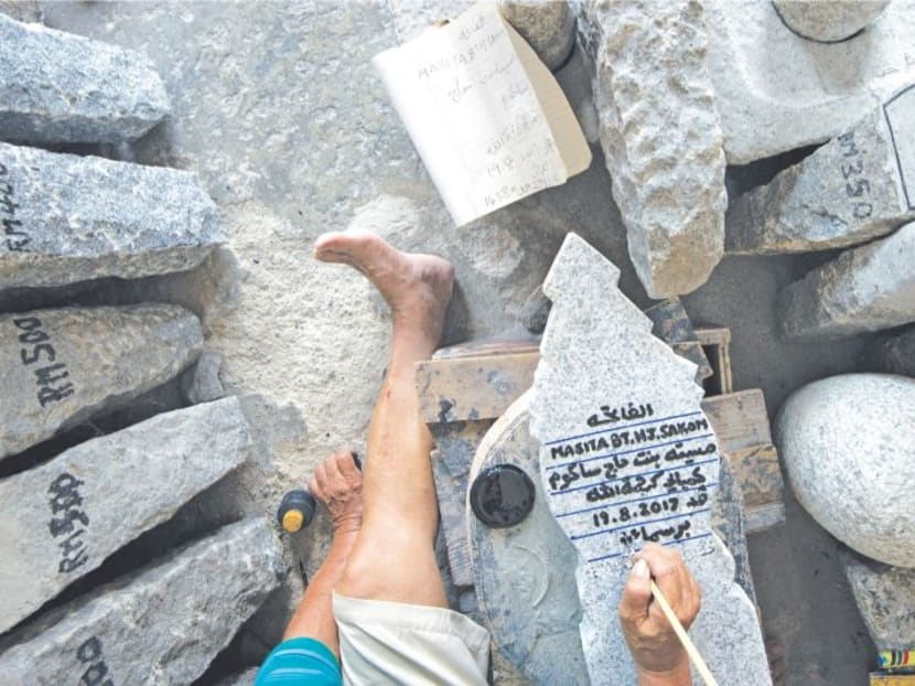 Mr Kuah seen here carving epitaphs using the calligraphy ink as a guideline to make deeper incisions for him to write over the inscription again so the ink stays. Photo: The Malay Mail.
