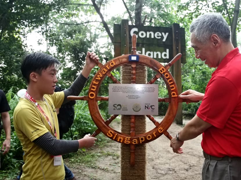 PM Lee, together with Tay Jing Xun, 15, an Outward Bound Singapore participant from North Vista Secondary School, mount the OBS nautical wheel on Coney Island to symbolise the expansion of the future use of the island by OBS. Photo: Nuria Ling/TODAY PM Lee, together with Tay Jing Xun, 15, an Outward Bound Singapore participant from North Vista Secondary School, mount the OBS nautical wheel on Coney Island to symbolise the expansion of the future use of the island by OBS. Photo: Nuria Ling/TODAY