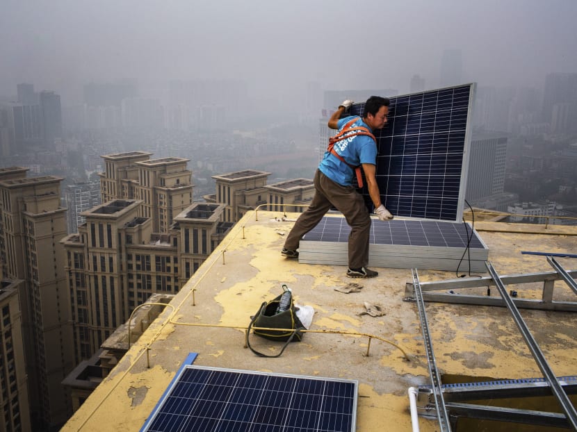 A worker installs solar panels atop a 47-storey high-rise in Wuhan, China. The greater consumption of utilities will lead to greater warming, unless societies can move away from fossil fuels to renewable types of energy, says the author.