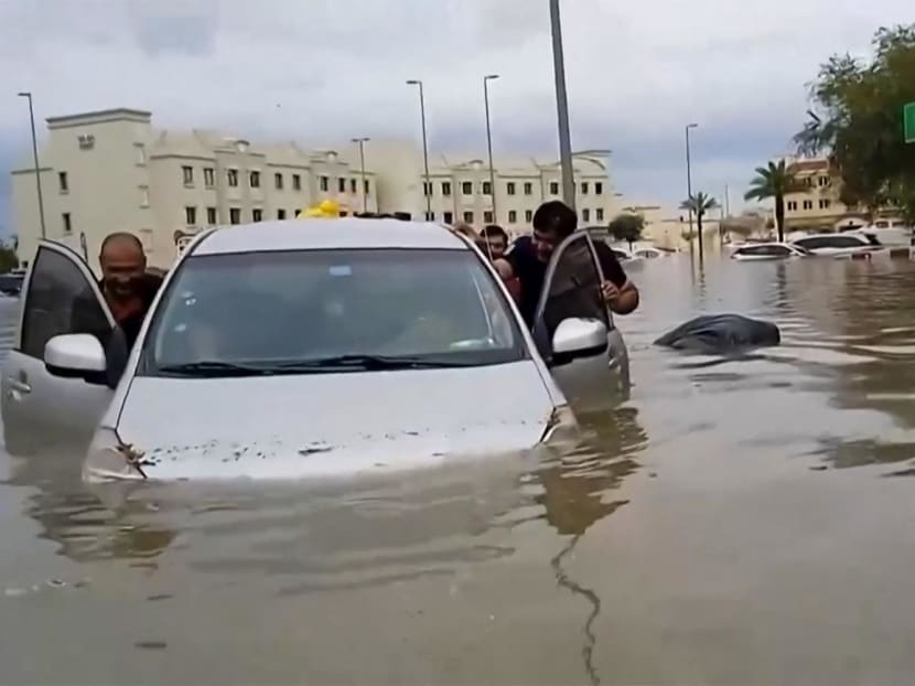 In this video grab from AFPTV, people push a stranded car along a flooded street in Dubai on April 16, 2024.