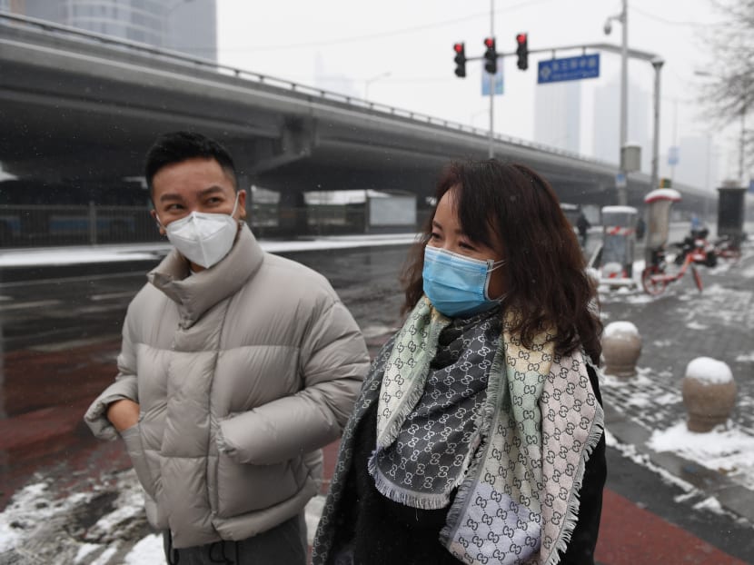 People wear masks as they walk in a deserted street in the central business district in Beijing on Feb 6, 2020.