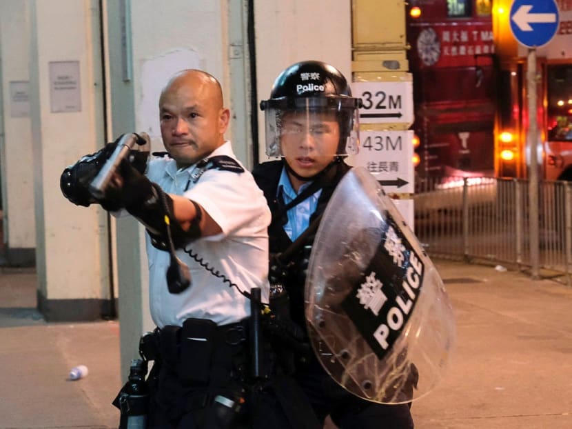 The officer, left, was filmed pointing a shotgun at protesters on July 30. He has been invited to the National Day celebrations on October 1 in Beijing.