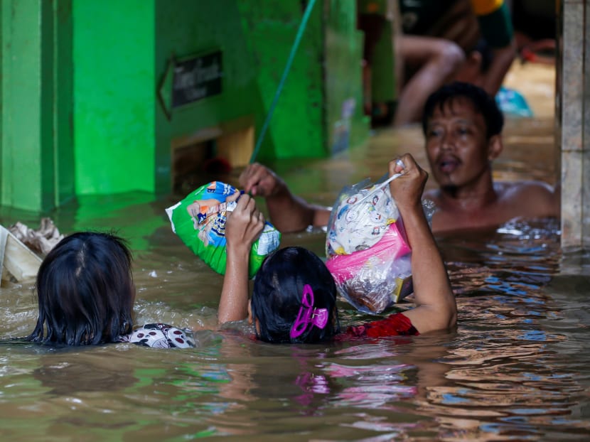 Women carry diapers as they cross an area flooded after heavy rains in Jakarta.