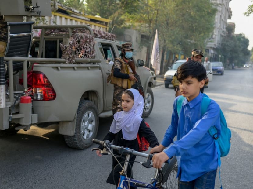 School children walk past Taliban special forces' personnel deployed along a road near the venue of a demonstration by women protestors outside a school in Kabul on Sept 30, 2021.