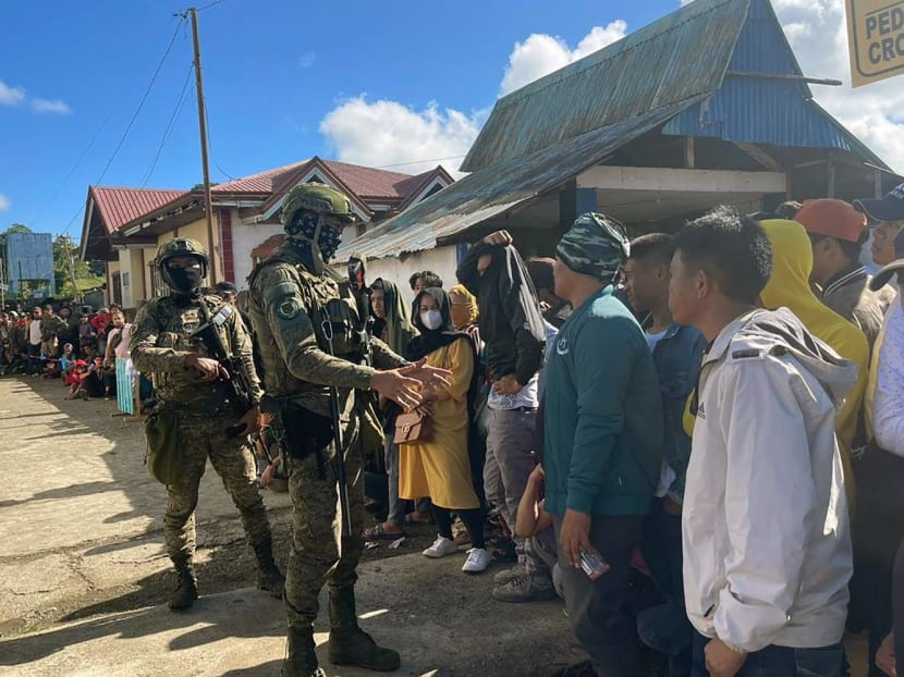 Soldiers stand guard as voters wait in line outside a polling station during the nationwide village and youth representative elections in Marawi, Mindanao island on Oct 30, 2023.