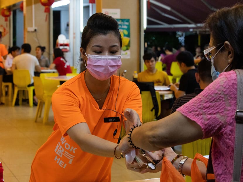 A worker at Keng Eng Kee Seafood handing takeaway food and disposable utensils to a customer.