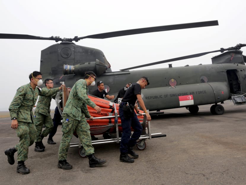 Members of Singapore's Air Force and Singapore's Civil Defence Force push a bambi bucket near a Chinook helicopter during preparation to fight forest fires on Oct 11, 2015. Photo: Reuters