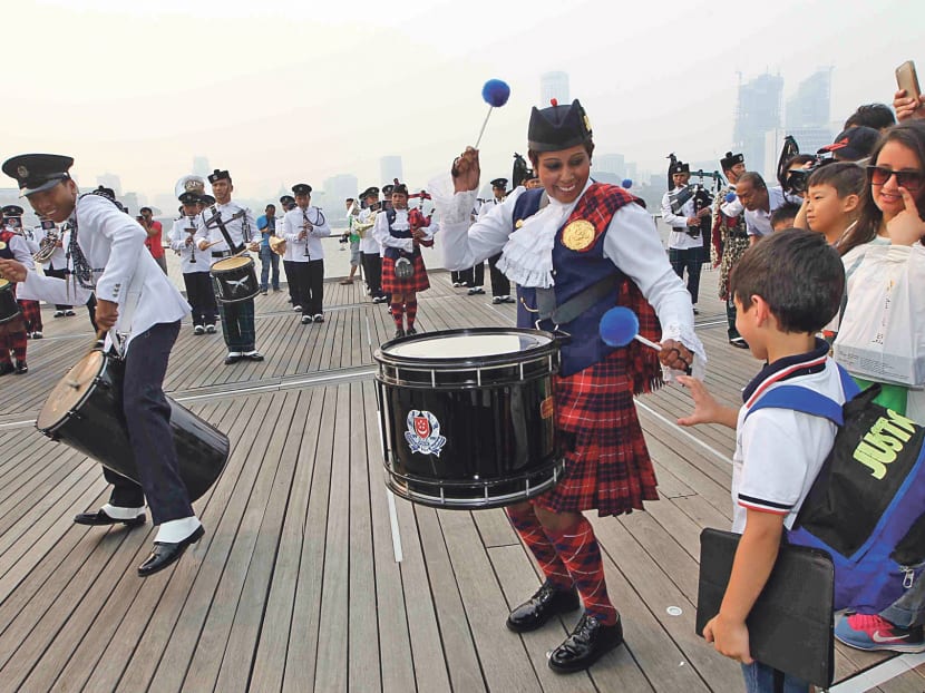 Sergeant Priya Vamen from the Singapore Police Force (SPF) Combined Band encouraging seven-year-old Abdul Aziz from Saudi Arabia, who was in the audience, to try his hand at the drums during a public performance by the SPF Combined Band at a street parade held at the Marina Bay Sands Waterfront Promenade yesterday. Photo: Ooi Boon Keong