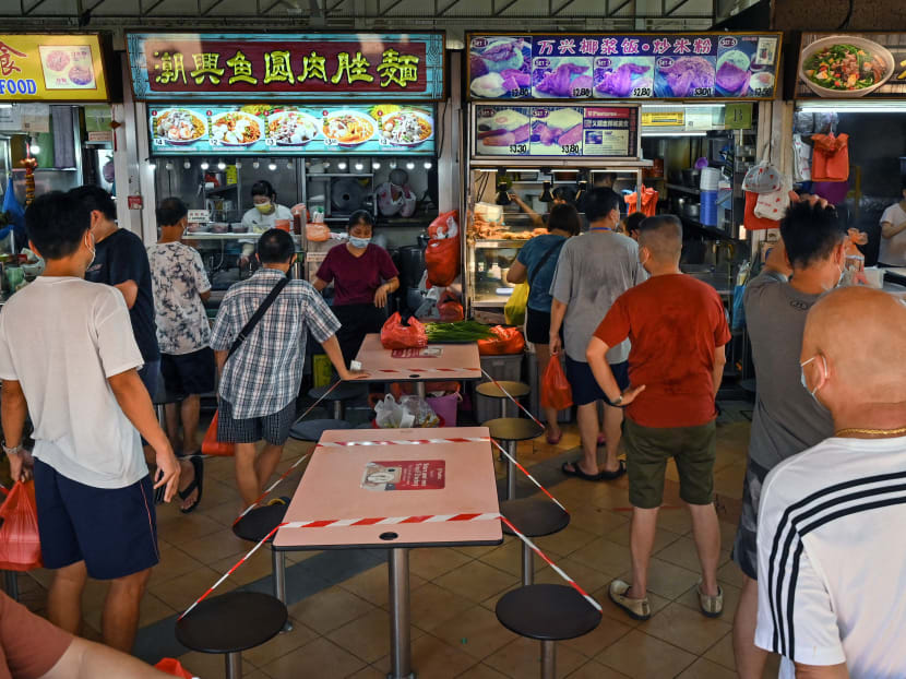 People queue to buy takeaway meals, as tables and chairs are cordoned off to prevent people from dining, at a hawker centre in Singapore on May 16, 2021.