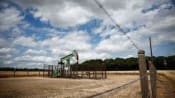 Oil edges down on easing Middle East risks but gains for a second month