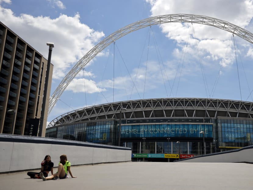 People rest in the sunshine in front of Wembley Stadium in London, UK on July 12, 2020, the day that Wembley should have hosted the Euro 2020 final.