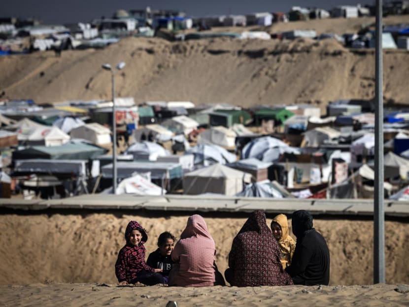 Displaced Palestinian women and children gather on a sand dune above a makeshift camp on the Egyptian border, west of Rafah in the southern Gaza Strip on Jan 14, 2024.