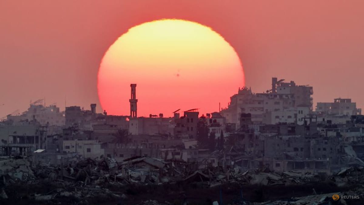 A large sun setting over a city skyline amidst rubble.