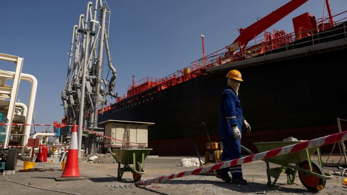 Worker in blue coveralls standing near a large ship at an industrial port.