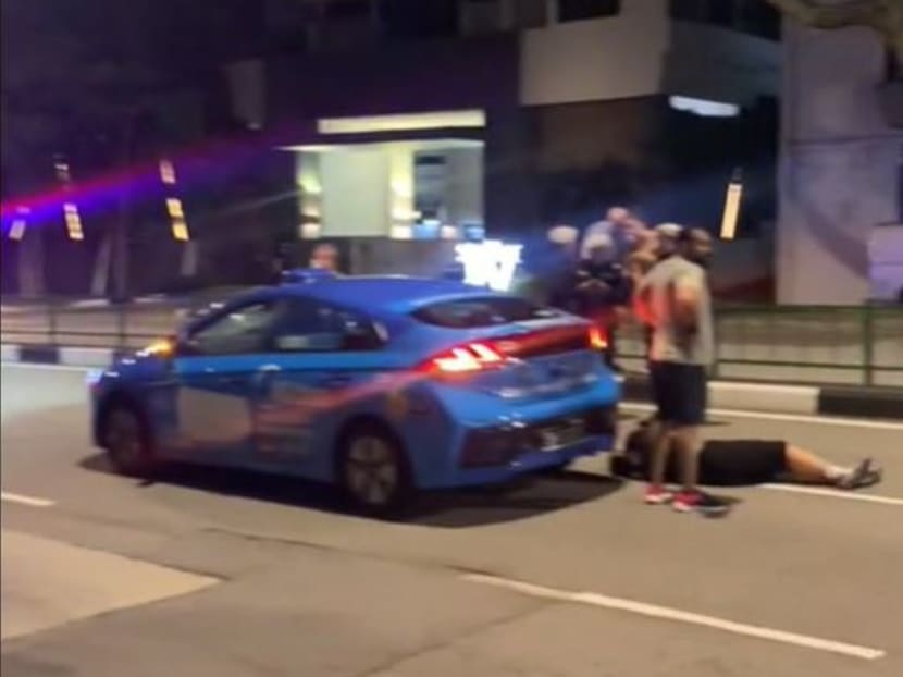 A screengrab of a video on TikTok showing a man lying by the rear wheel of a blue ComfortDelGro taxi. A screengrab of a video on TikTok showing a man lying by the rear wheel of a blue ComfortDelGro taxi.