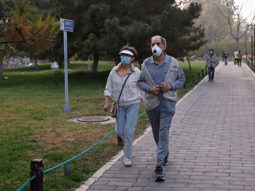 People wearing face masks walk in a park as Beijing issues orange alert for heavy air pollution, in Beijing, China October 31, 2023. 